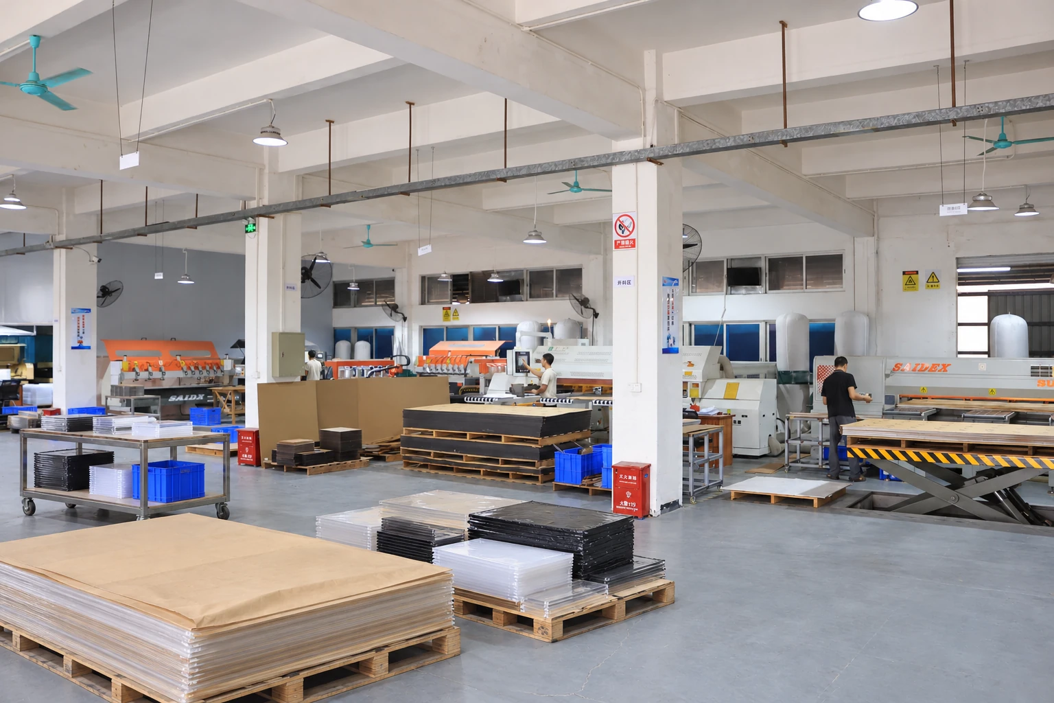 Acrylic sheets stacked on pallets beside cutting equipment and material preparation workstations