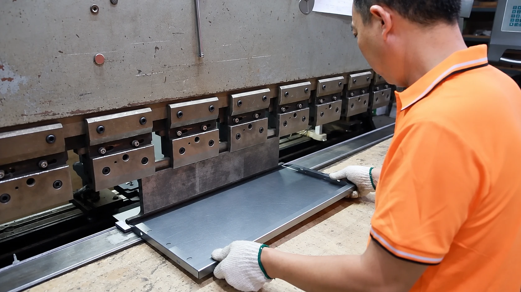 Gloved operator positioning a metal panel under a press brake